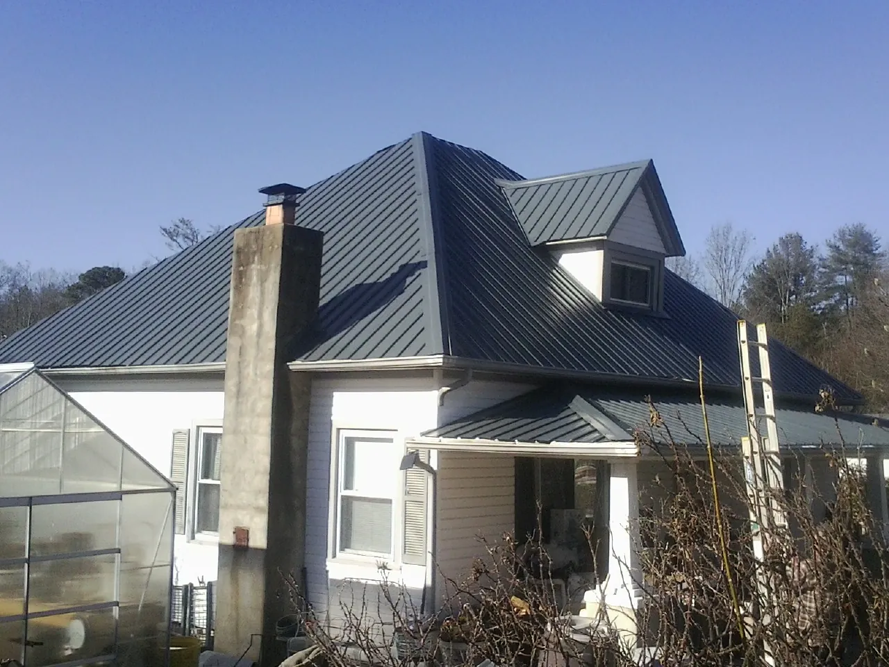 Dark blue standing seam metal roof on a white farmhouse with dormer — Slate & Tile Roof Repair by Roofing Brothers in Earth City