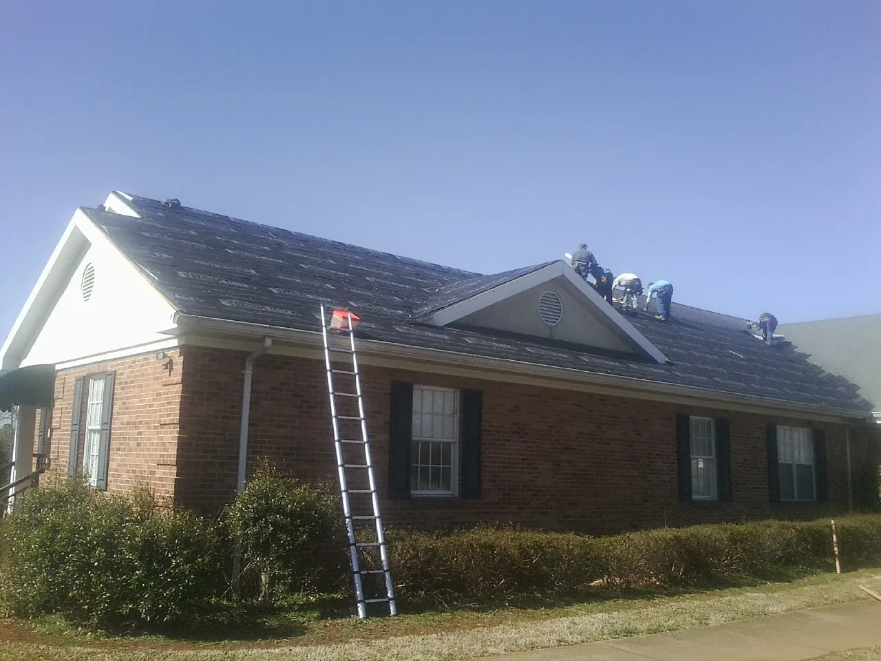 Crew tearing shingles off a brick ranch roof with a ladder set — Metal Roof Repair work by our crew in Earth City