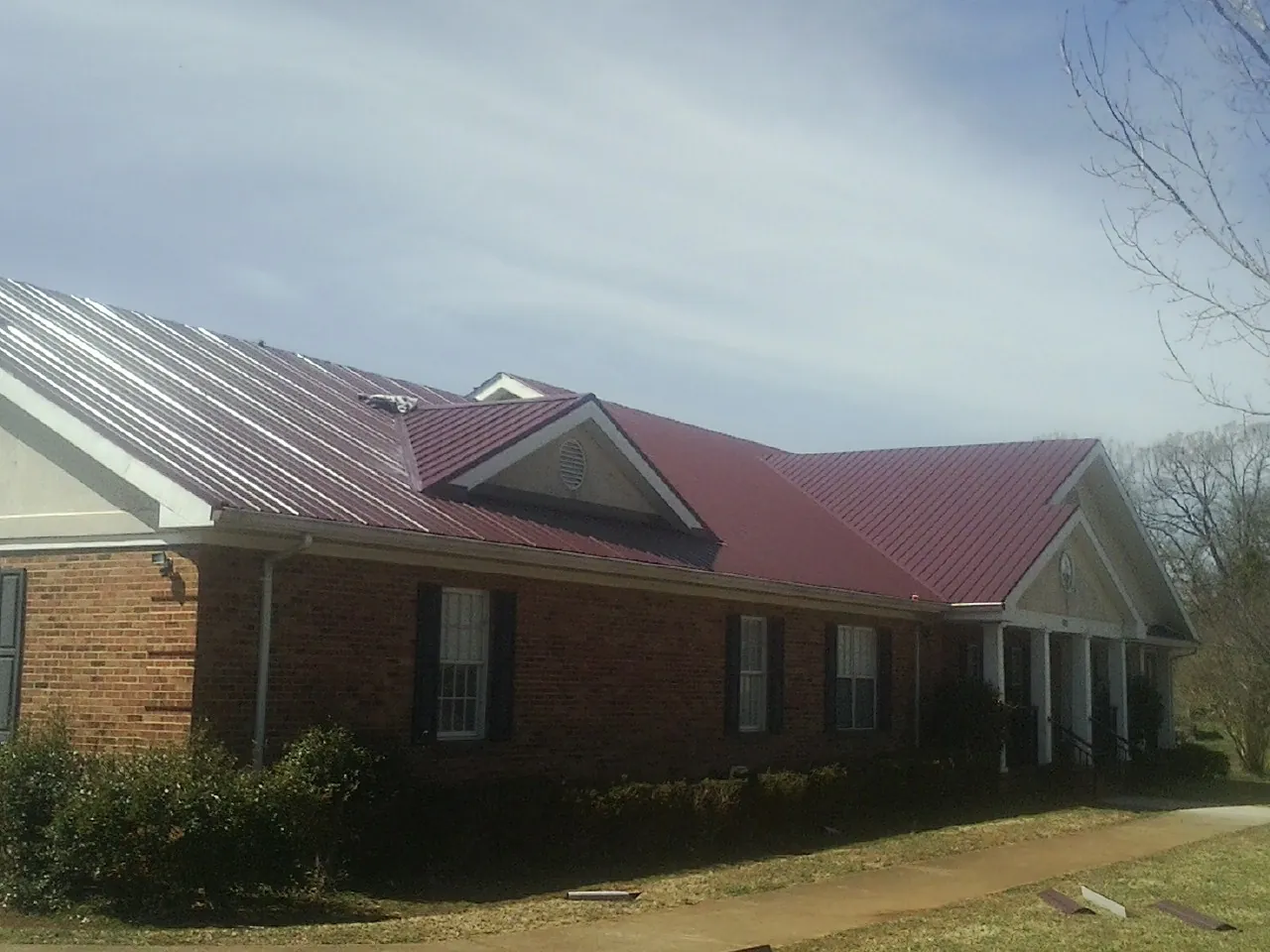 Red metal roof with gabled entries on a long brick building, from a Hail Damage Roof Repair job in Earth City