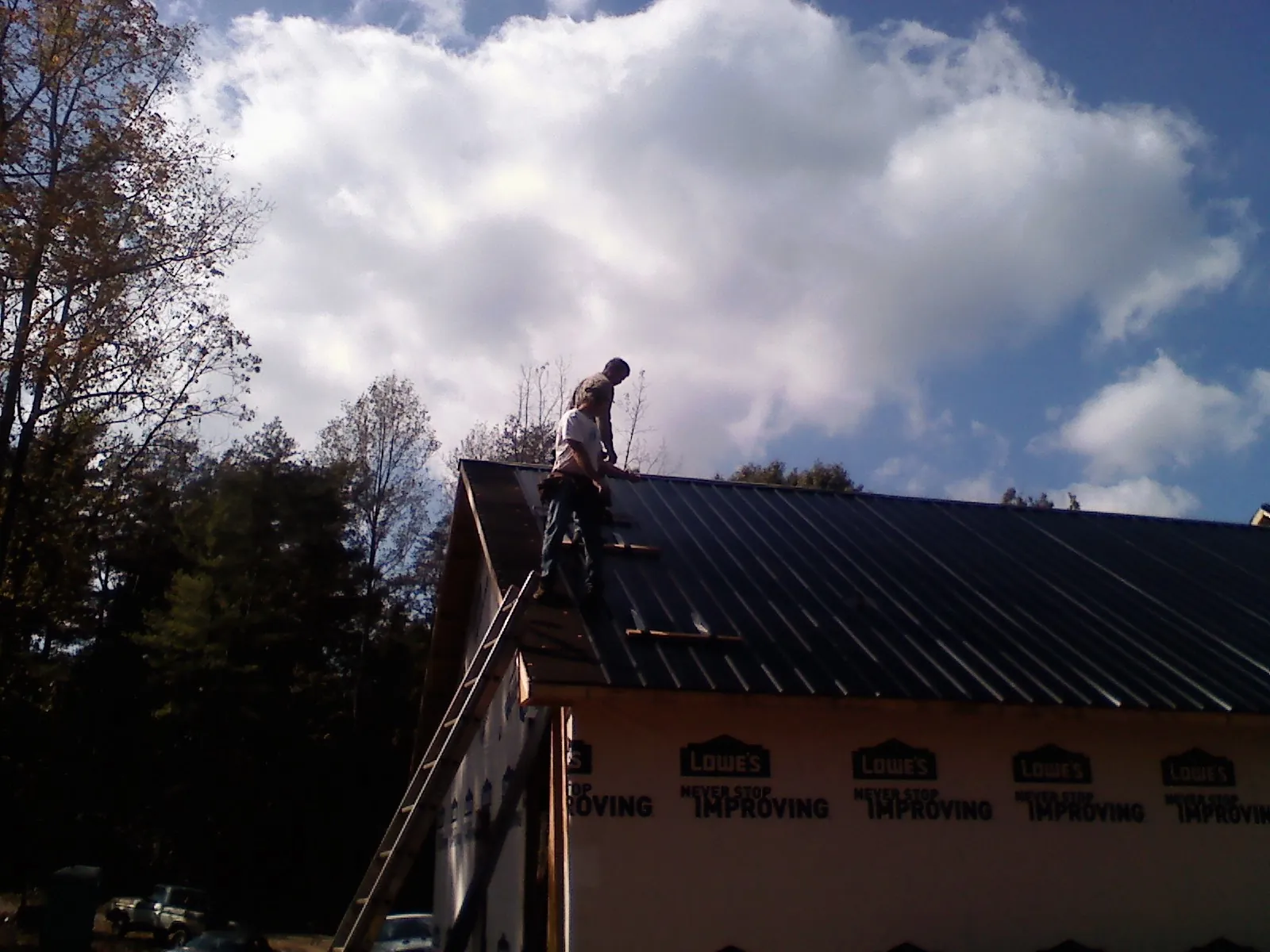Roofer fastening dark metal panels high against a cloudy sky, from a Roof Inspection job in Earth City