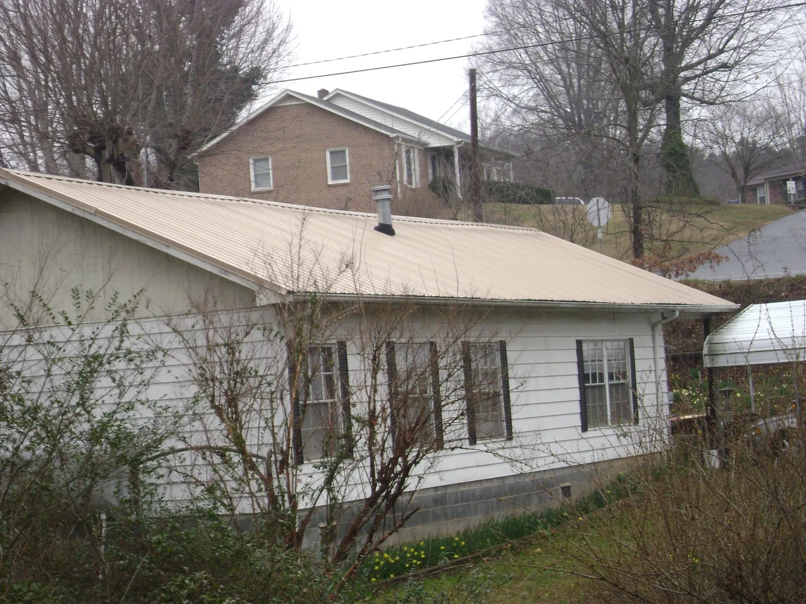 Tan metal roof on a white sided house set into a hillside — Commercial Roofing by Roofing Brothers in Earth City